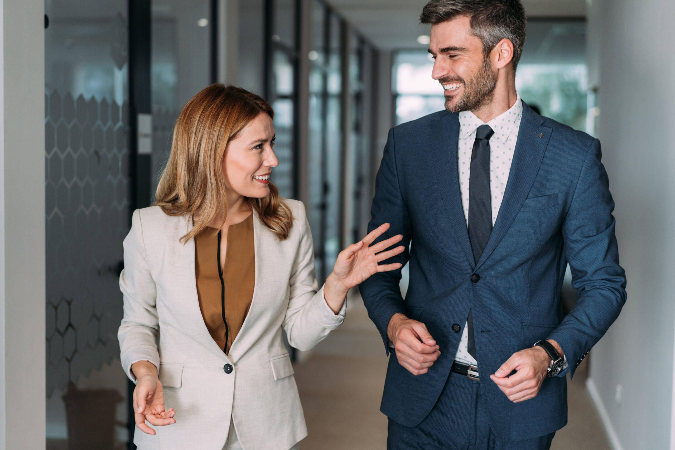 Shot of two colleagues having a discussion in modern office. Confident business people working together in the office. Corporate business persons discussing new project and sharing ideas while walking in office corridor.